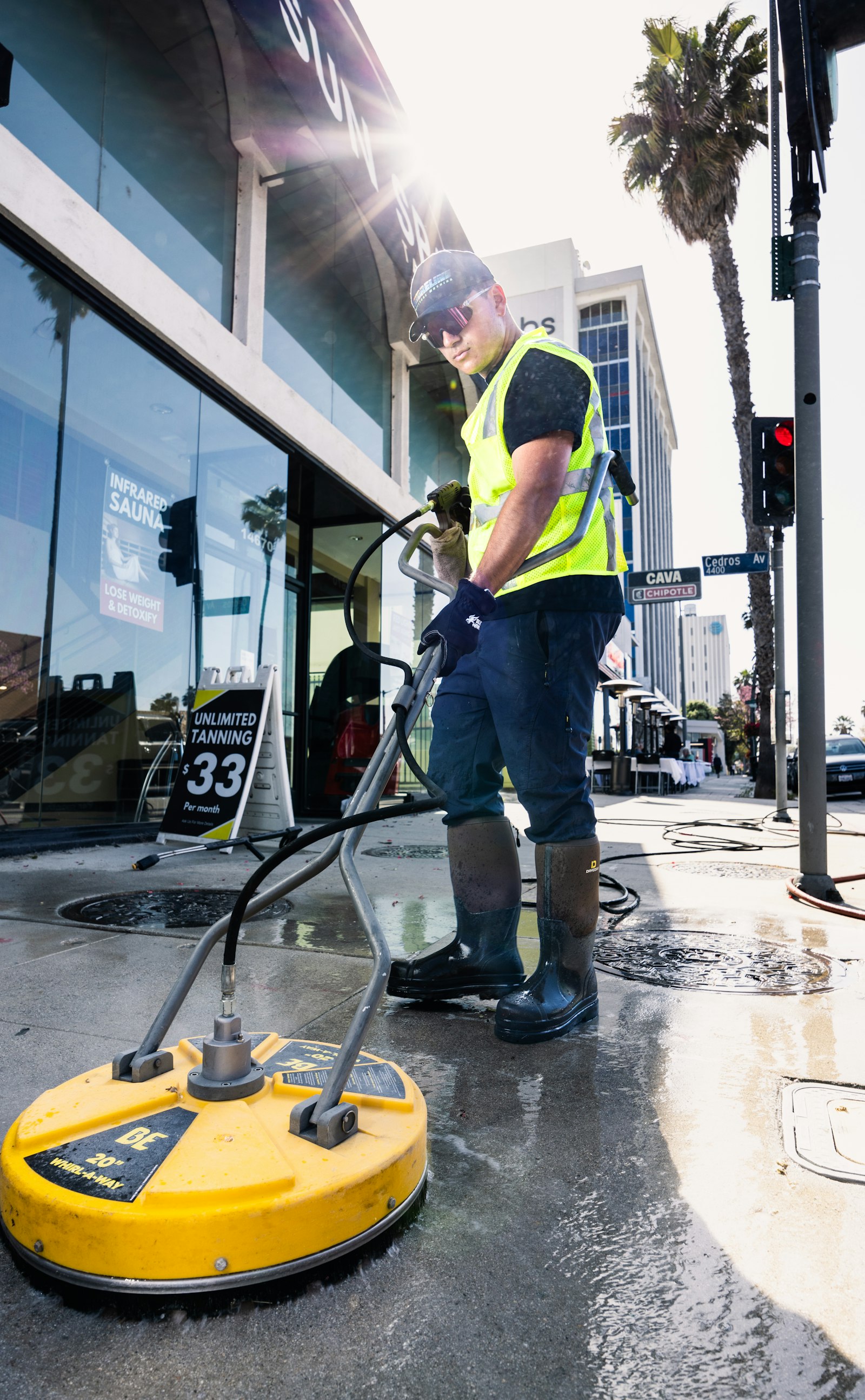 Worker in safety vest pressure-washing a concrete sidewalk